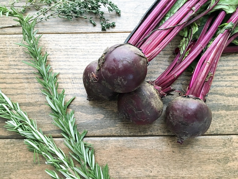 bunch of red beets next to herbs.