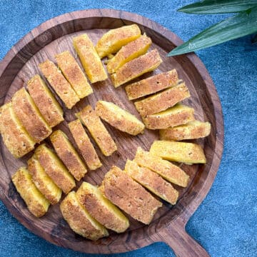 sliced brazilian pinepple on round wooden tray.