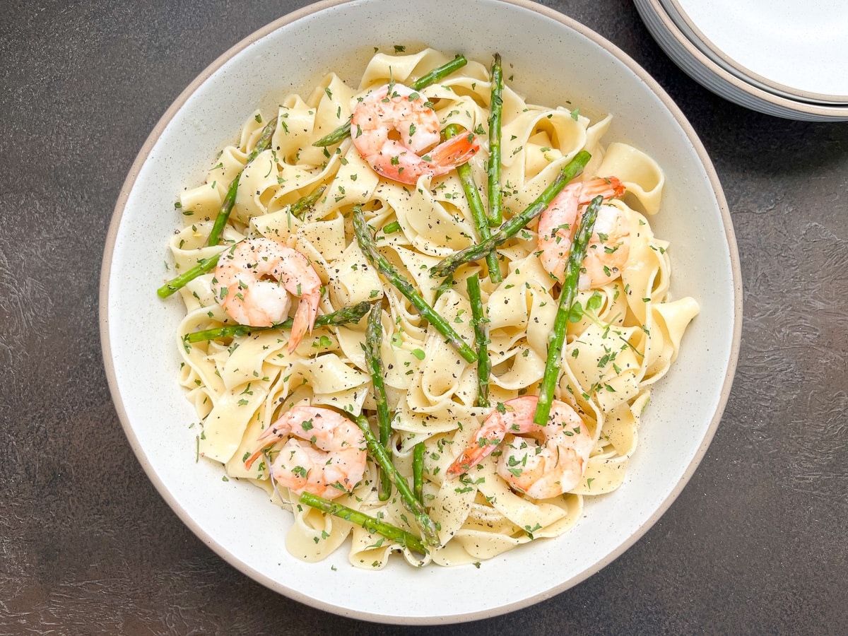 shrimp and asparagus pasta in white bowl with image centered in middle of backdrop.