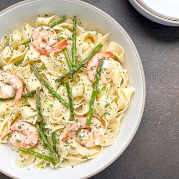 close up of shrimp and asparagus pasta in white bowl.