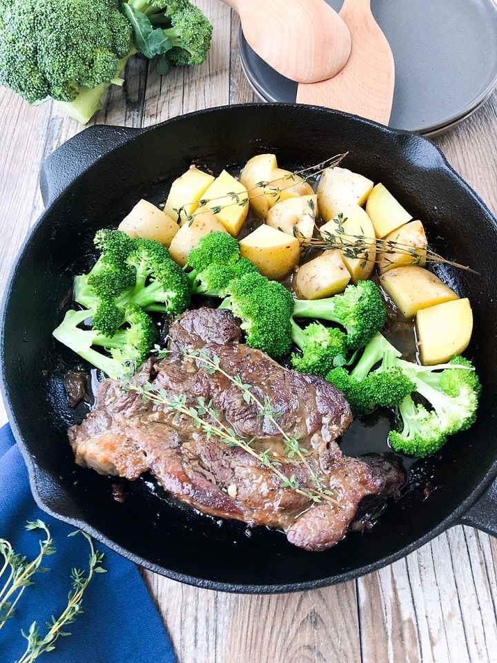 oven baked chuck roast recipe in skillet with veggies next to gray plates and wooden spoons