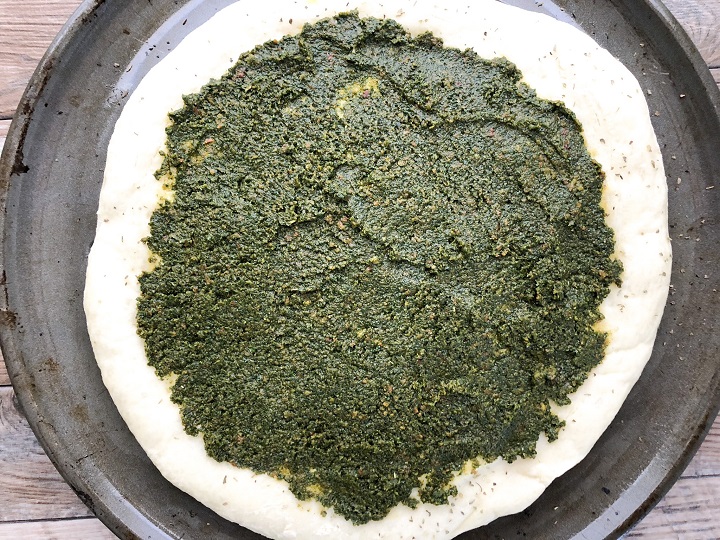 pesto sauce spread across pre-baked pizza dough