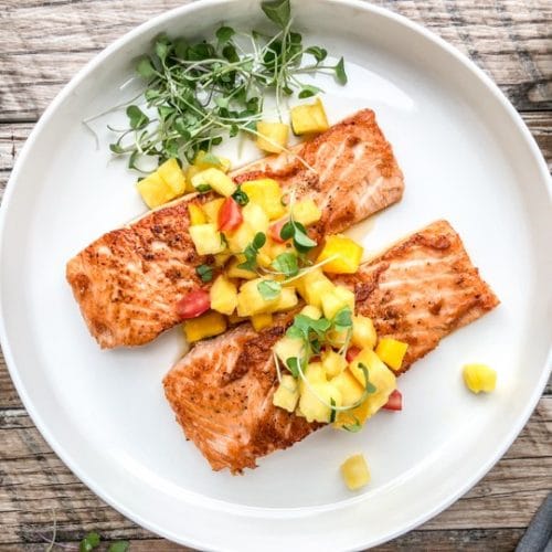 pan seared salmon on a white plate with microgreens