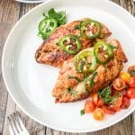 baked mediterranean chicken breast served on a white plate with roasted tomatoes