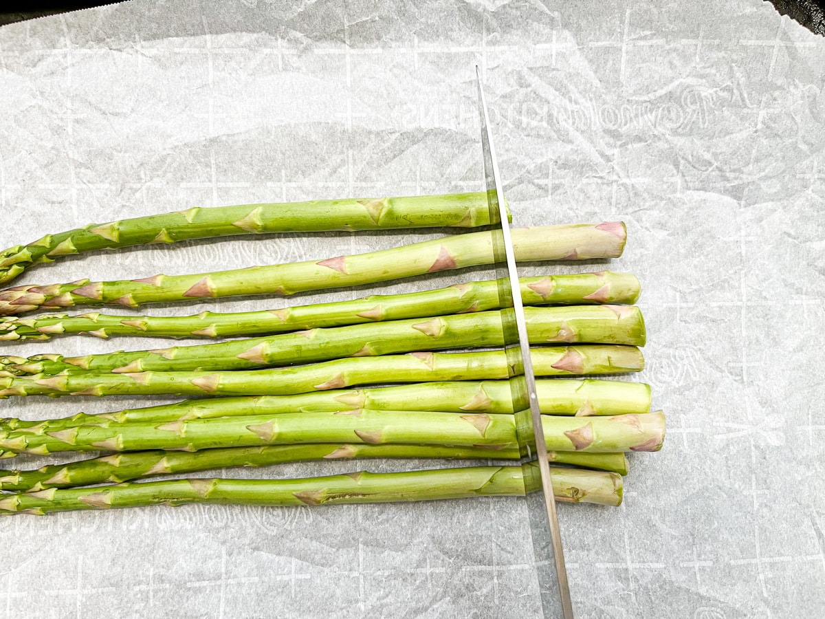 asparagus on parchment paper with ends ready to be cut.