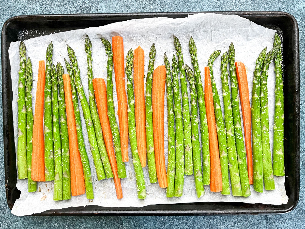 asparagus and carrots arranged on baking sheet with parchment paper.