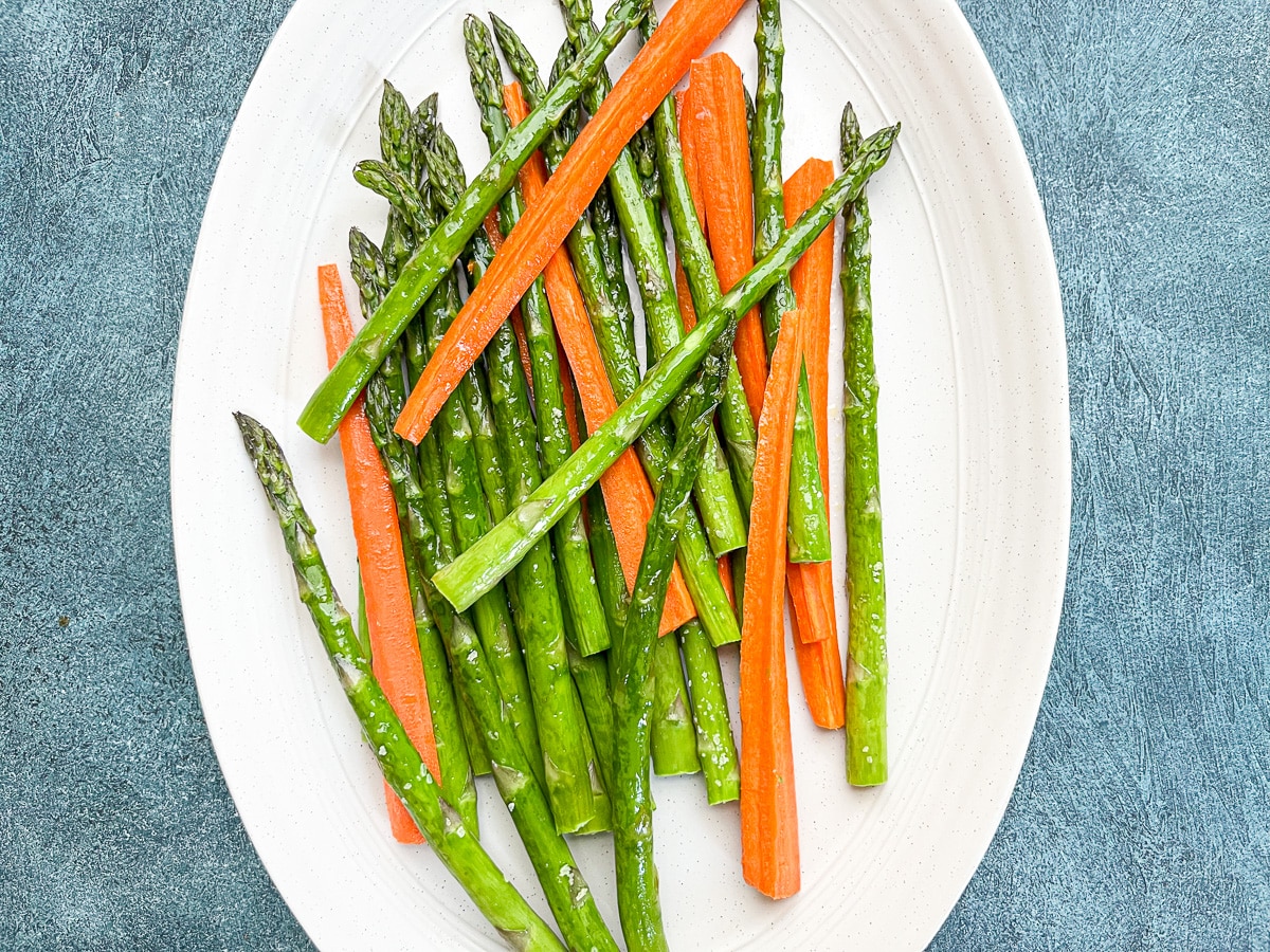 overhead shot of asparagus and carrots on white serving dish.