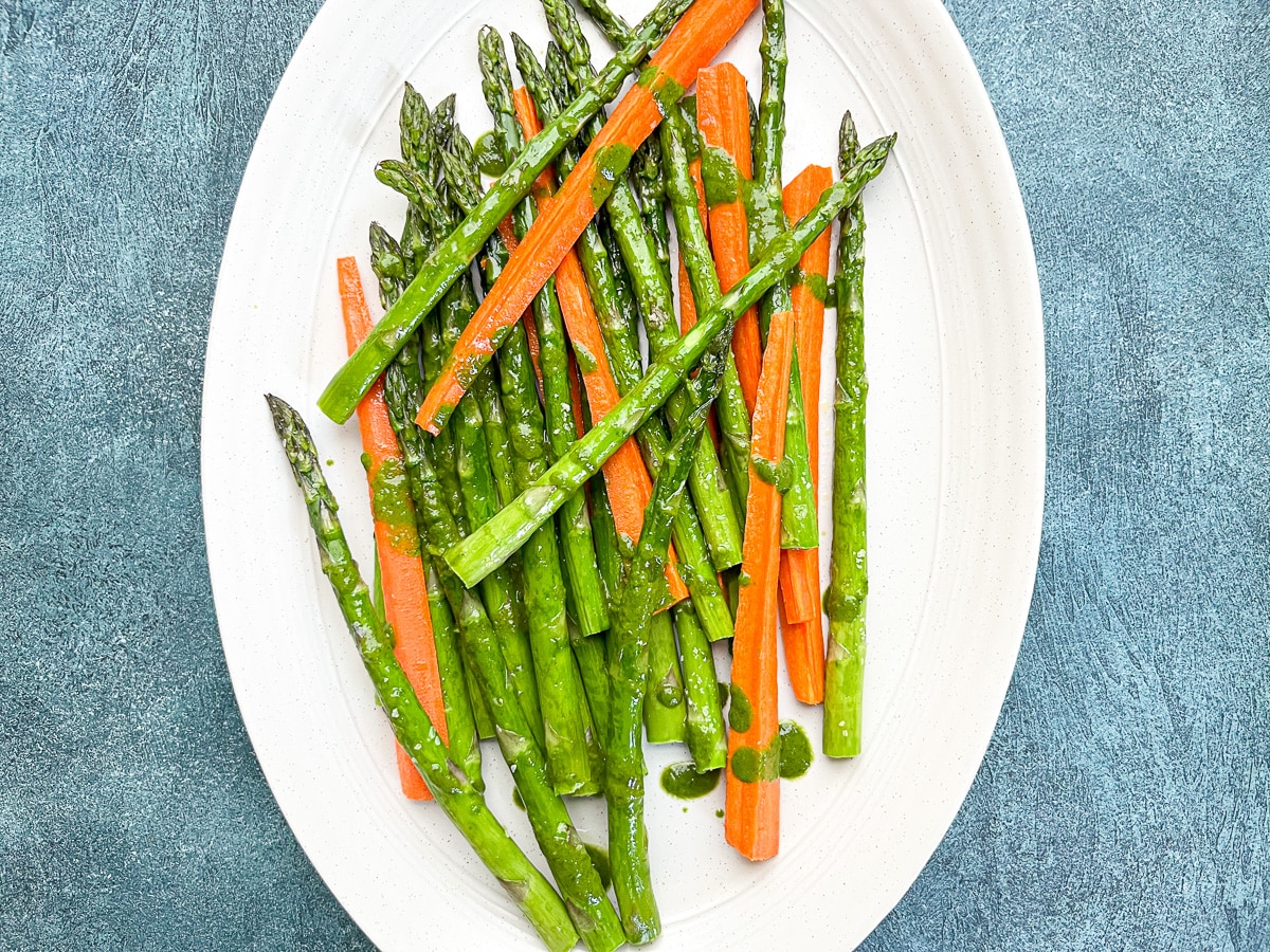 overhead shot of asparagus and carrots on white serving dish drizzled with basil vinaigrette.