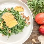 simple arugula salad with nectarines served on a while plate garnished with pecans and sliced nectarines