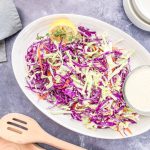 healthy coleslaw recipe no mayo in a cream colored serving bowl with a side of tahini salad dressing