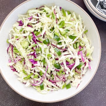 coleslaw in white bowl next to 2 small salad bowls that are stacked with striped napkin inside one bowl.