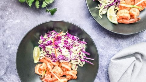 shrimp bowl recipe served in a black bowl with green and purple cabbage and tahini dressing