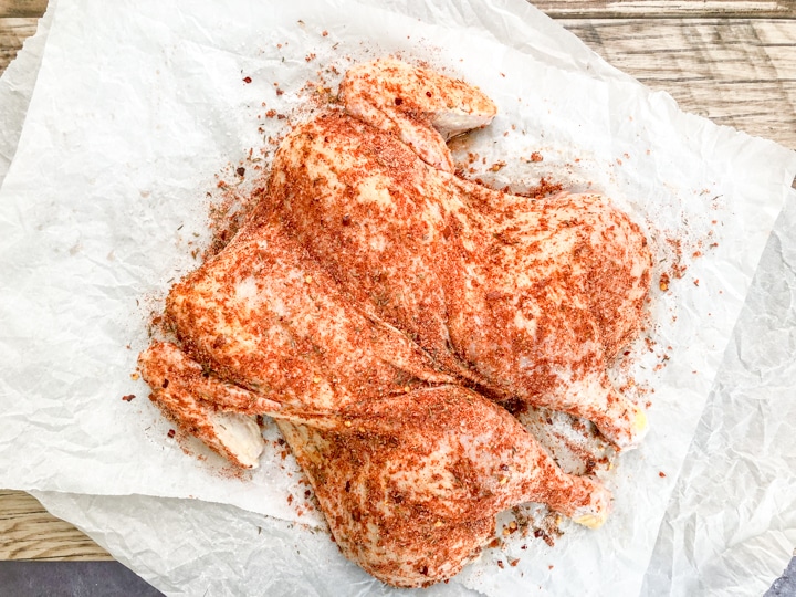 spatchcock chicken that's raw on top of parchment paper seasoned with Cajun spices