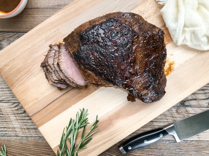 tri tip cut into slices on wooden chopping board with knife on side 