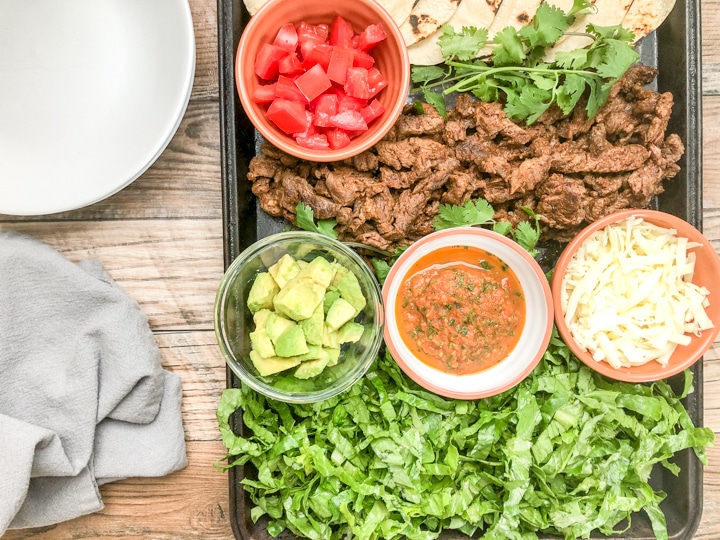 ingredients for soft taco recipe on baking sheet with white plates on side