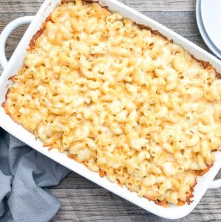 creamy baked mac and cheese in a white casserole dish with plates on side