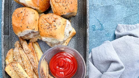 Overhead shot of turkey sliders in an oval gray tray with fries and ketchup next to gray napkin.