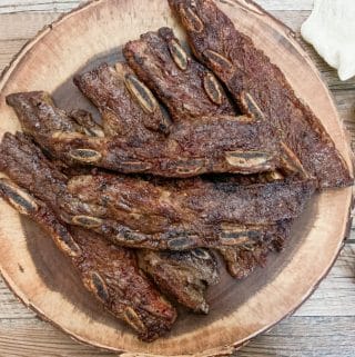 grilled flanken ribs served on a circular wooden serving dish next to a beige napkin