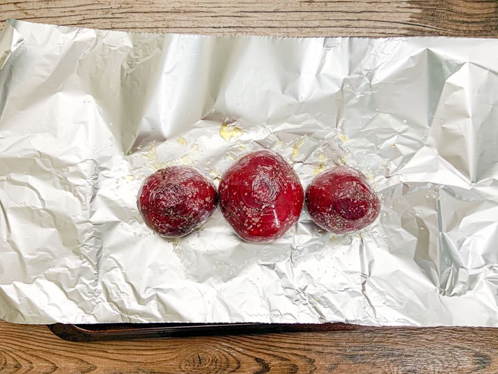 3 raw beets sitting on top of foil paper drizzed with extra virgin olive oil and kosher salt