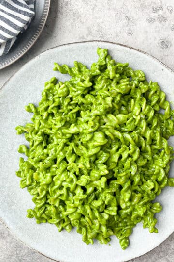 pesto pasta in large light gray plate next to smaller gray plate that has a striped gray napkin on top of it.