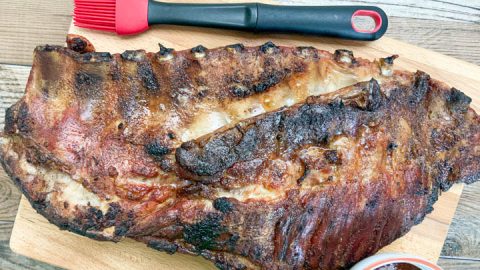 slab of grilled pork spare ribs on cutting board with sauce