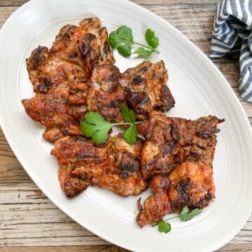 grilled chicken thighs served on oval white platter garnished with cilantro leaves