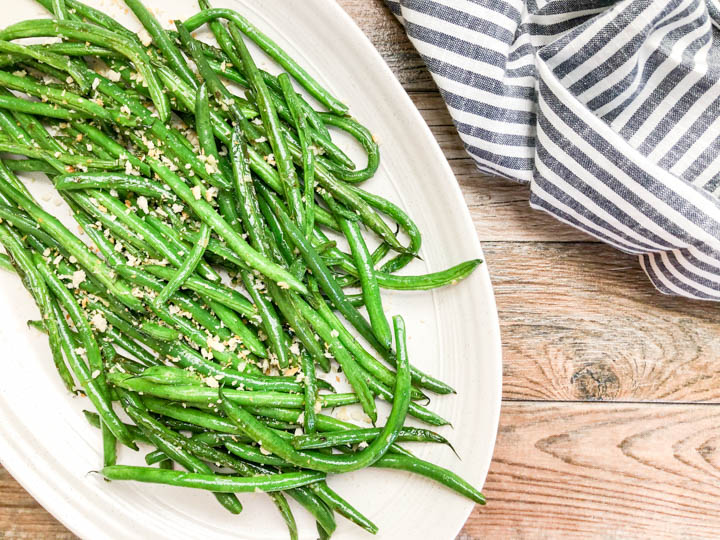 close up of green beans topped with toasted panko crumbs with fresh herbs on white dish