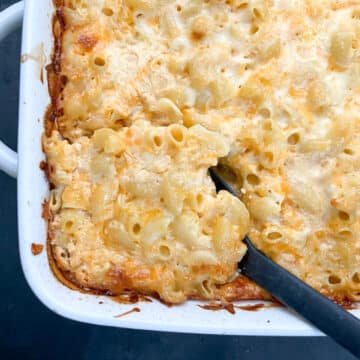 Baked Soul Food mac and cheese in a white baking dish with a black serving spoon lifting a cheesy corner.