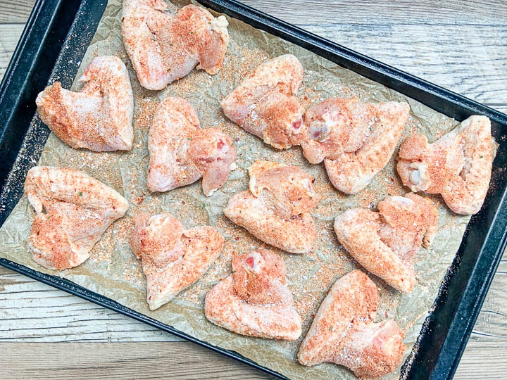 seasoned chicken wings on top of baking sheet with parchment paper