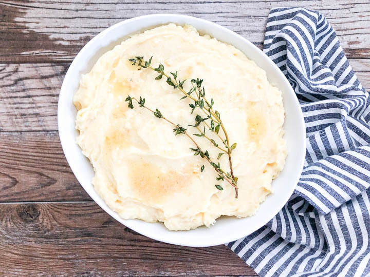 garlic mashed potatoes garnished with butter and herbs in white serving bowl
