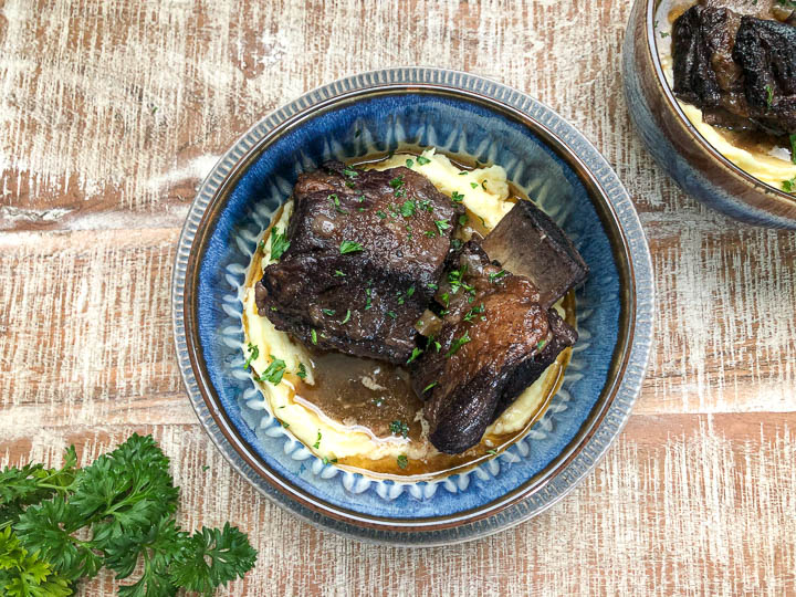 over head shot of braised short ribs in blue bowl with garnish