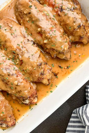 smothered turkey wings in a white baking dish next to a striped napkin.