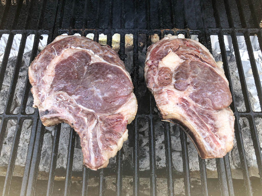 ribeye steaks on grill grates of a charcoal grill
