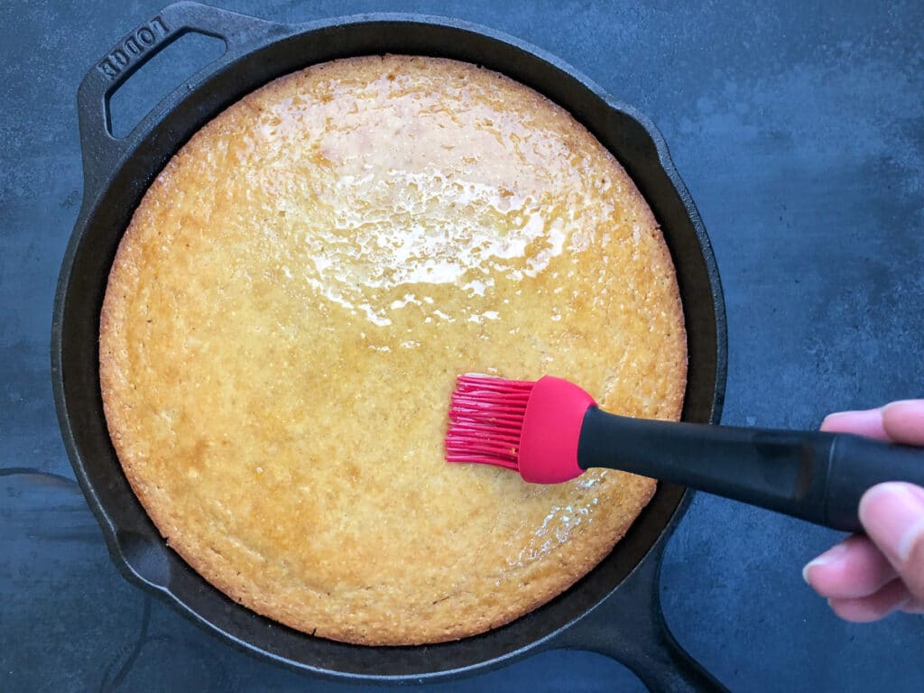 cake cornbread with lemony simple syrup being brushed with pastry brush.