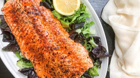 broiled salmon sitting on bed of lettuce on white plate