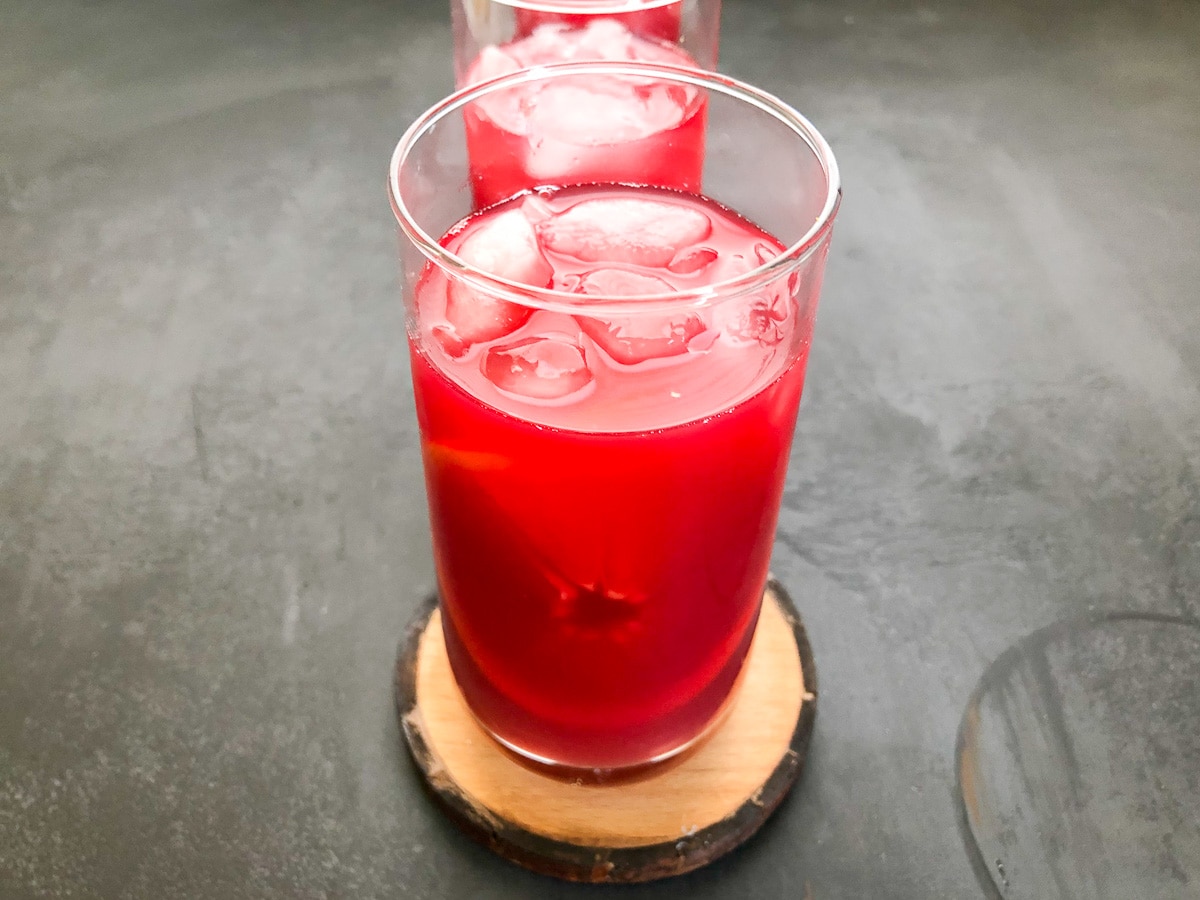 close up photo of hibiscus drink garnished with cara cara orange slice in glass.