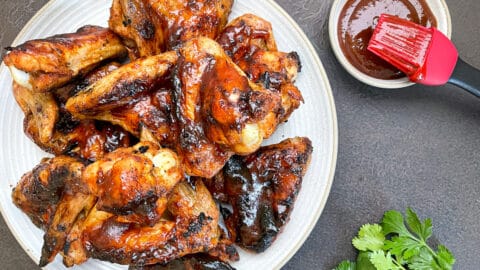 charcoal grilled chicken wings on white plate next to dipping bowl with bbq sauce.