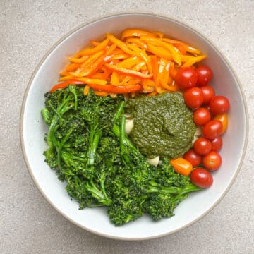 pasta and veggies in white bowl with pesto before mixing.