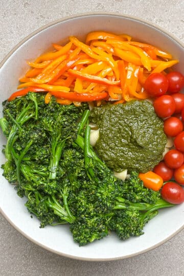 pasta and veggies in white bowl with pesto before mixing.