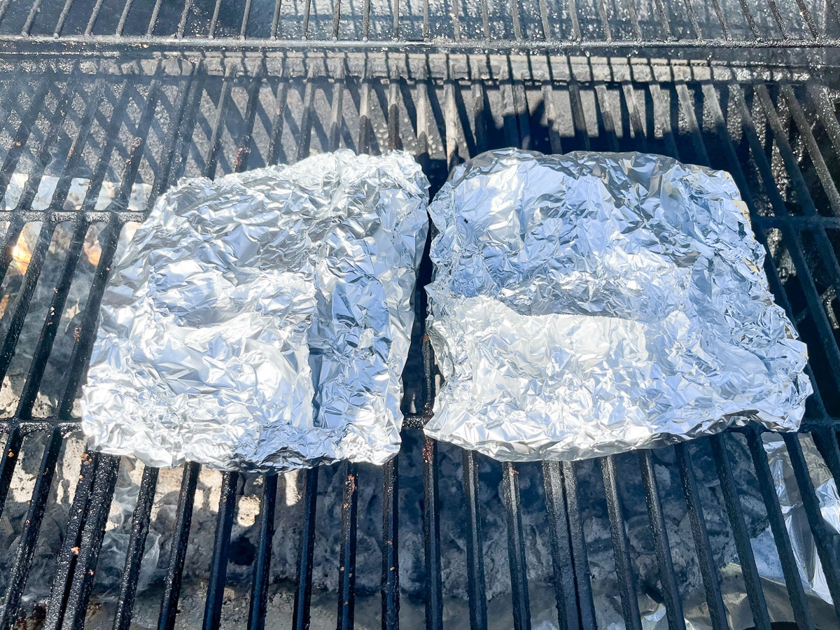 chuck roast wrapped in foil on grill grates.