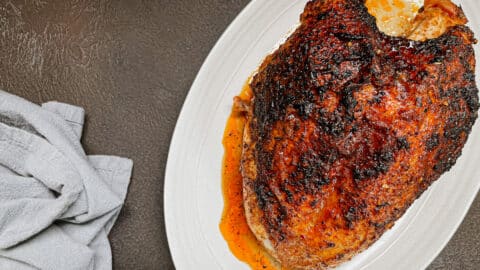 cajun turkey breast resting on white platter next to gray napkin.