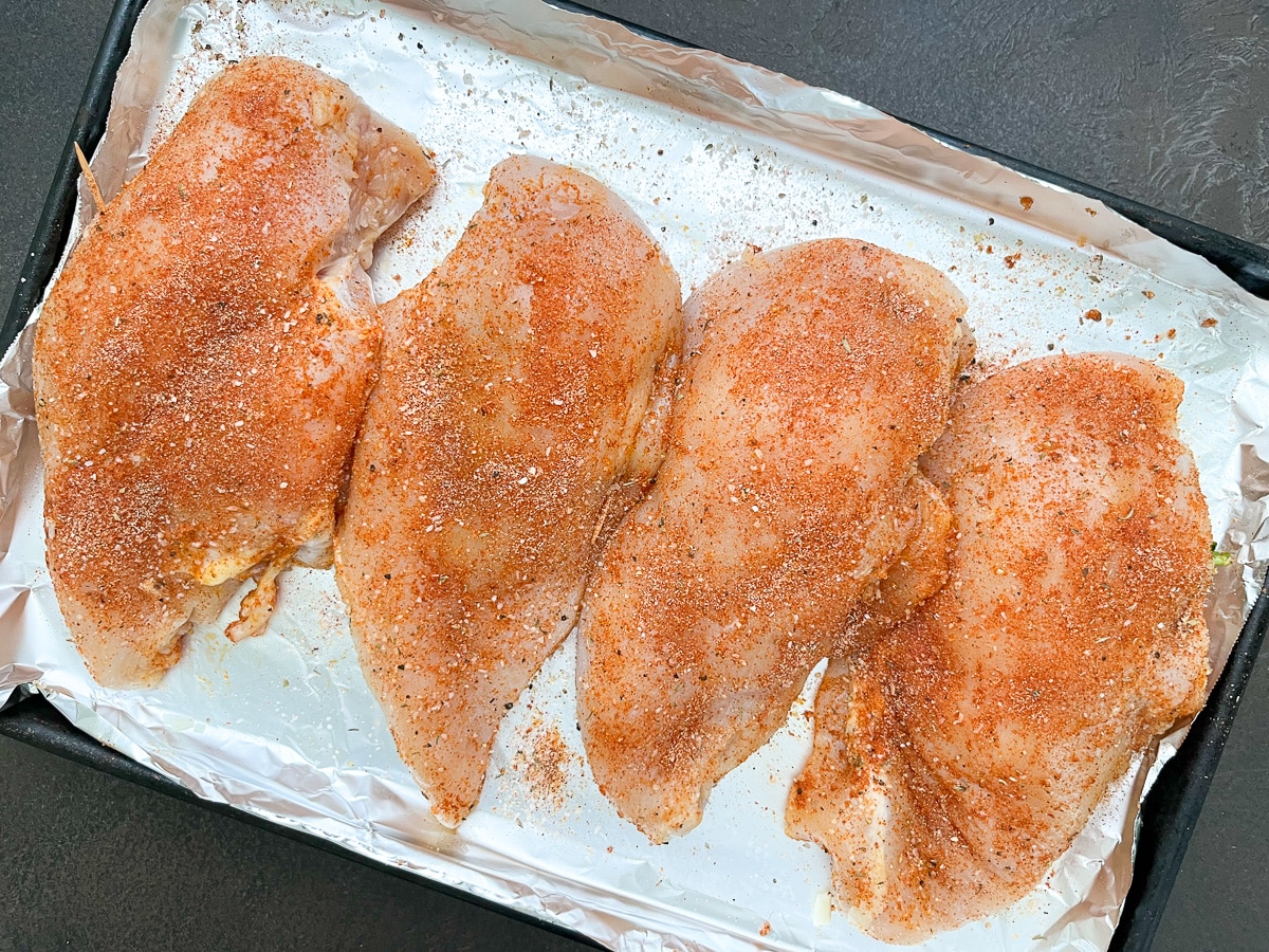 Seasoned chicken breast on baking sheet line with foil paper.