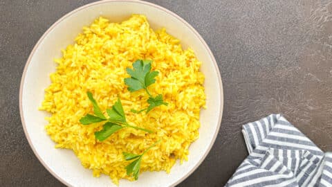 yellow rice in white bowl with parsley garnich next to striped napkin.