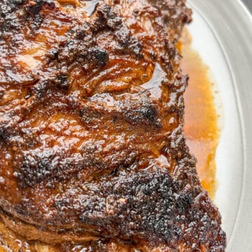 Close-up of whole tri-tip on a white serving tray with pan juices spooned over the top and dripping down the sides.
