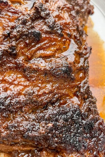Close-up of whole tri-tip on a white serving tray with pan juices spooned over the top and dripping down the sides.