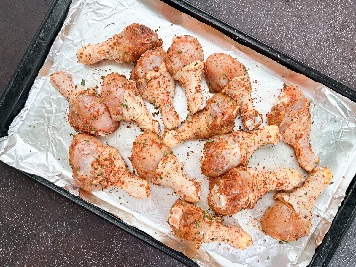 seasoned chicken legs on baking sheet before being placed on charcoal grill.