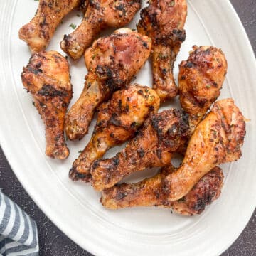 close-up shot of grilled chicken legs on white oval serving tray.