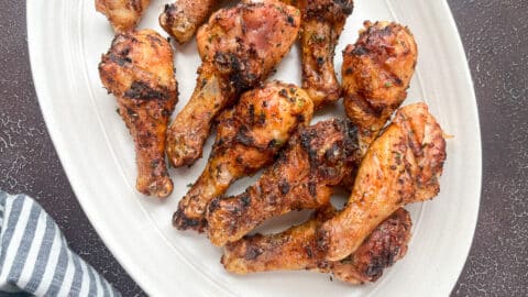 close-up shot of grilled chicken legs on white oval serving tray.
