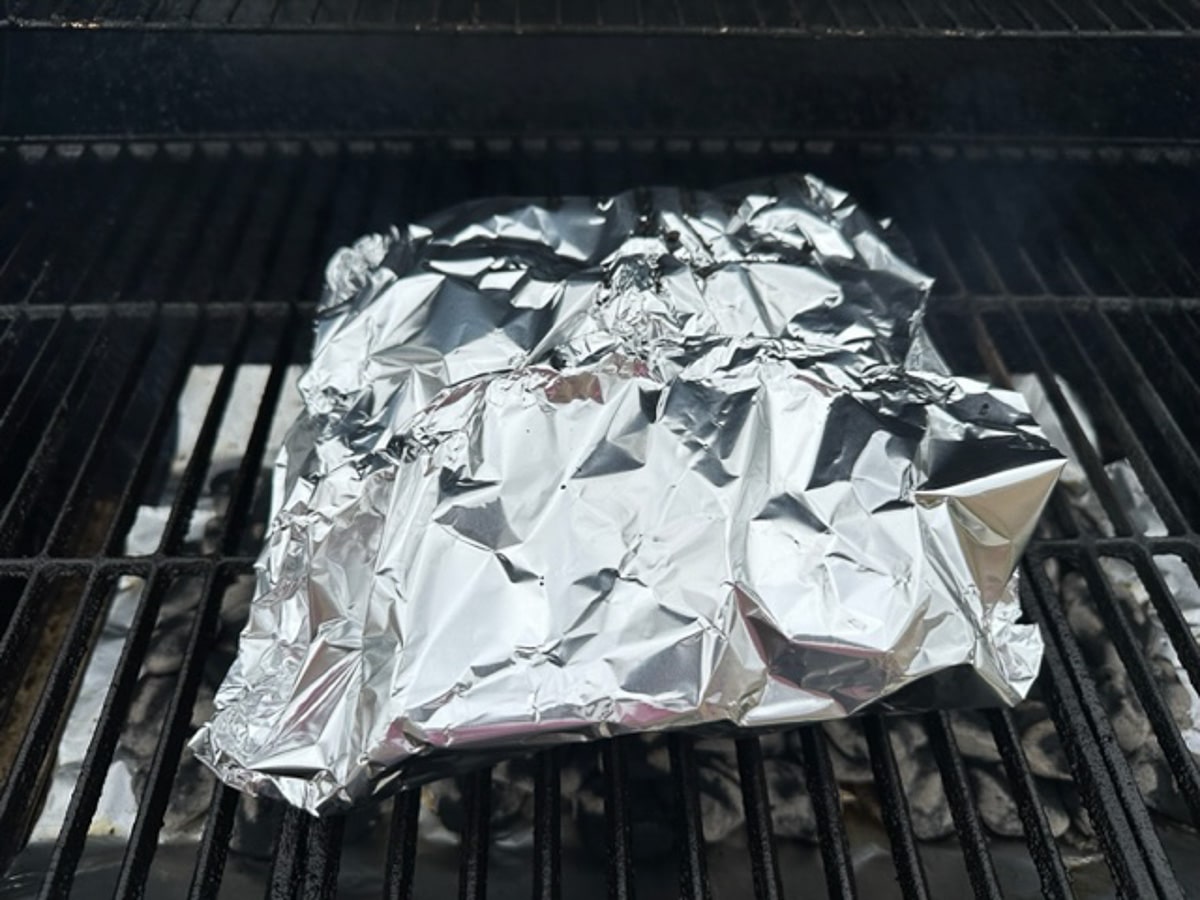 tri-tip wrapped in foil sitting on grill grates.