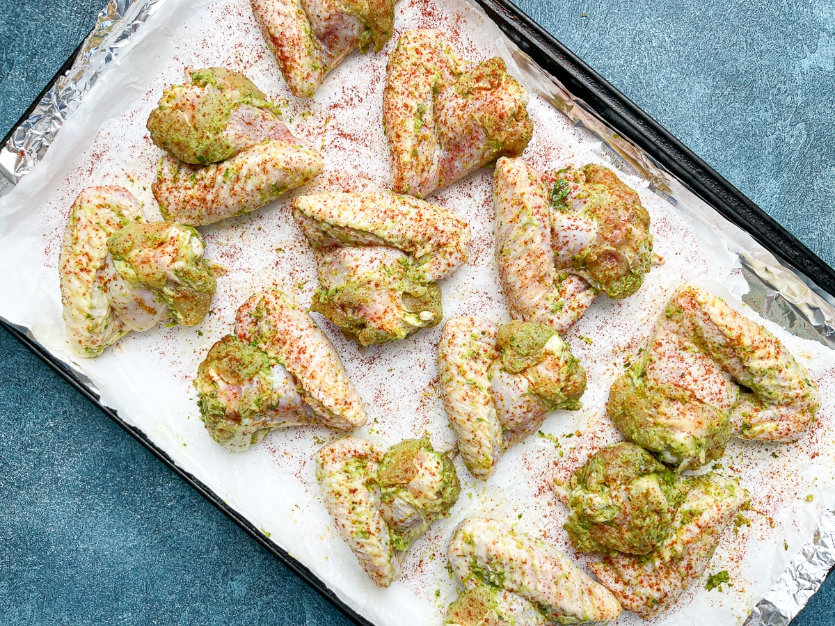 raw marinated chicken wings on baking sheet lined with parchment paper.